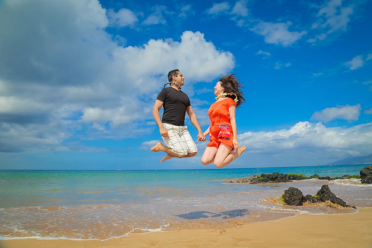 Couple jumping on the beach under a bright blue sky